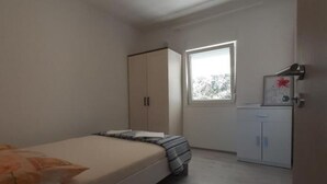 A bedroom with a bed, a wardrobe, a small cabinet, and a window.