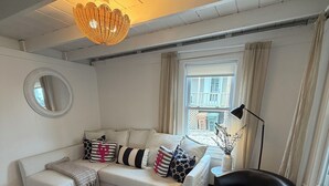 Ein modernes Wohnzimmer mit einer Couch, einem schwarzen Ledersessel, einem runden Spiegel und einem Fenster mit Vorhängen.