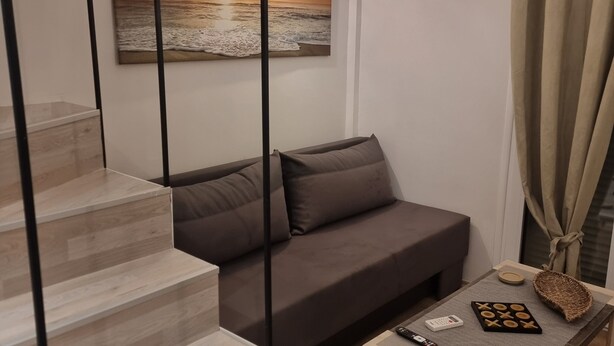 A modern living room with a staircase, a sofa, a coffee table with board games, and a wall clock.