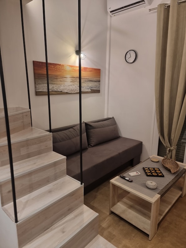 A modern living room with a staircase, a sofa, a coffee table with board games, and a wall clock.