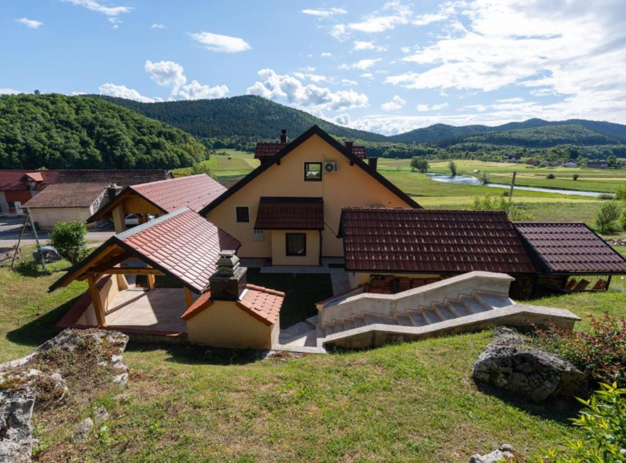 A traditional chalet-style building with a steeply pitched roof, surrounded by a lush green landscape and mountains in the background.