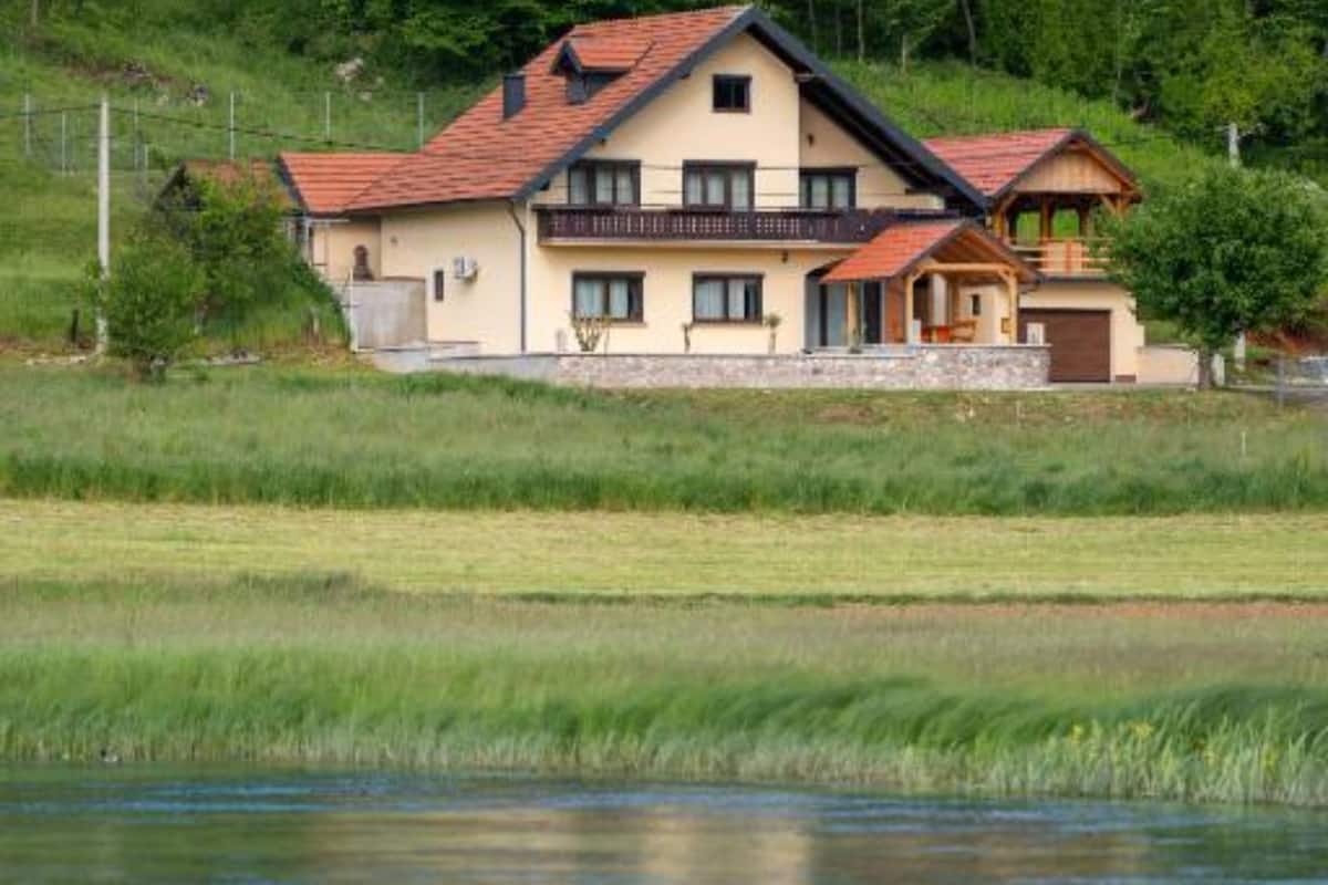 A two-story house with a red-tiled roof, a balcony, and a pond in the foreground.