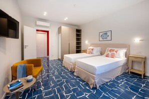 A hotel room with two beds, a TV, a sofa, a small table with a book, and a patterned floor. - Elegant & Modern 4Bedroom Home in Central Sorrento (Sorrento)