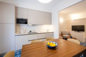A modern kitchen with a microwave, stove, and sink. There is a dining area with a wooden table and chairs, and a TV mounted on the wall.