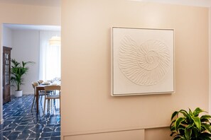 A framed artwork of a spiral shell on a wall, a dining area with a table and chairs, and a potted plant.