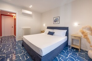 A bedroom with a large bed, a bedside table, a wall-mounted air conditioner, and a radiator.