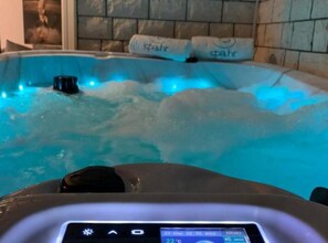 A hot tub with blue lighting, a control panel, and two towels labeled 'spahr'.