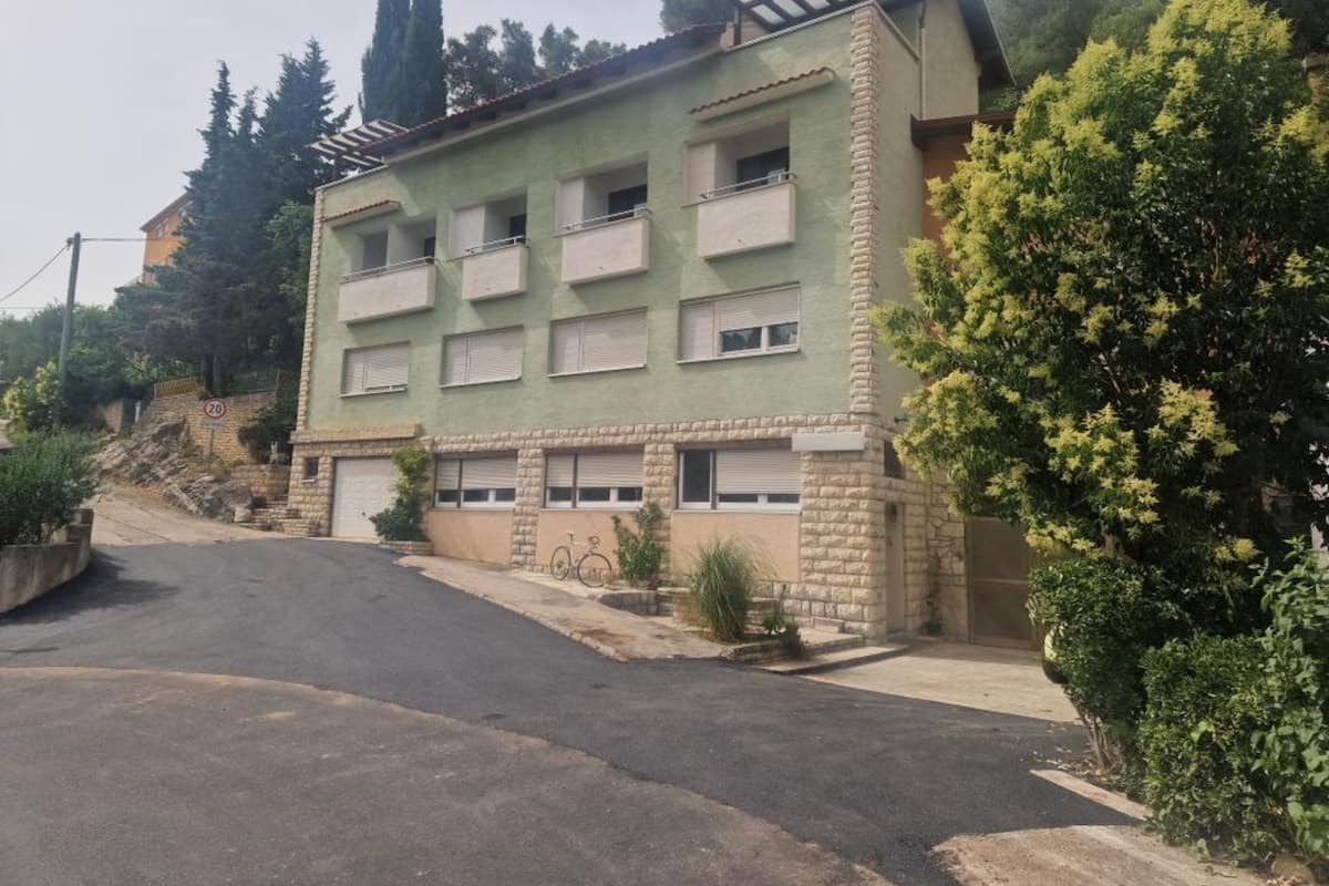 A multi-story building with a flat roof, a balcony on the second floor, and a garage door.