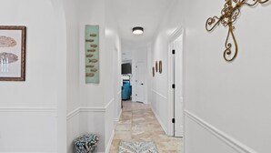 A hallway with white walls, a patterned rug, a fish-themed artwork, and a decorative metal piece. - Beach House - Baby Blue Heron by PHG (Panama City Beach)