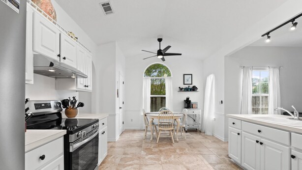 A spacious kitchen with white cabinetry, a black stove, and a dining area with a table and chairs. - Beach House - Baby Blue Heron by PHG (Panama City Beach)