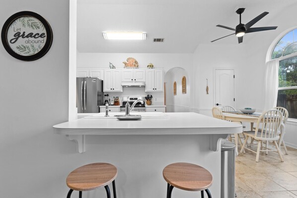A modern kitchen with white cabinetry, a central island, and a dining area with wooden chairs.