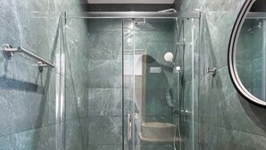 Un baño moderno con ducha de vidrio, tocador de madera y un espejo redondo.