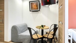 A modern room with a grey sofa, a small round table with two chairs, a flat-screen TV mounted on the wall, and a bed with a white headboard. - Hoche A 11 - Two Bedroom Apartment, Sleeps 5 (Paris)