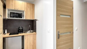 A compact kitchen with a microwave, coffee maker, and sink. There is a small refrigerator and wooden cabinets. A wooden door with a handle is visible. - Hoche A 11 - Two Bedroom Apartment, Sleeps 5 (Paris)