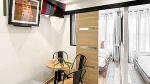 A modern room with a bed, a dining area with a table and chairs, and a large window with curtains. - Hoche A 11 - Two Bedroom Apartment, Sleeps 5 (Paris)