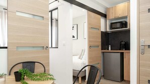 A modern kitchen with a microwave, coffee maker, and refrigerator. There is a dining area with a table and chairs, and a bed in the background. - Hoche A 11 - Two Bedroom Apartment, Sleeps 5 (Paris)