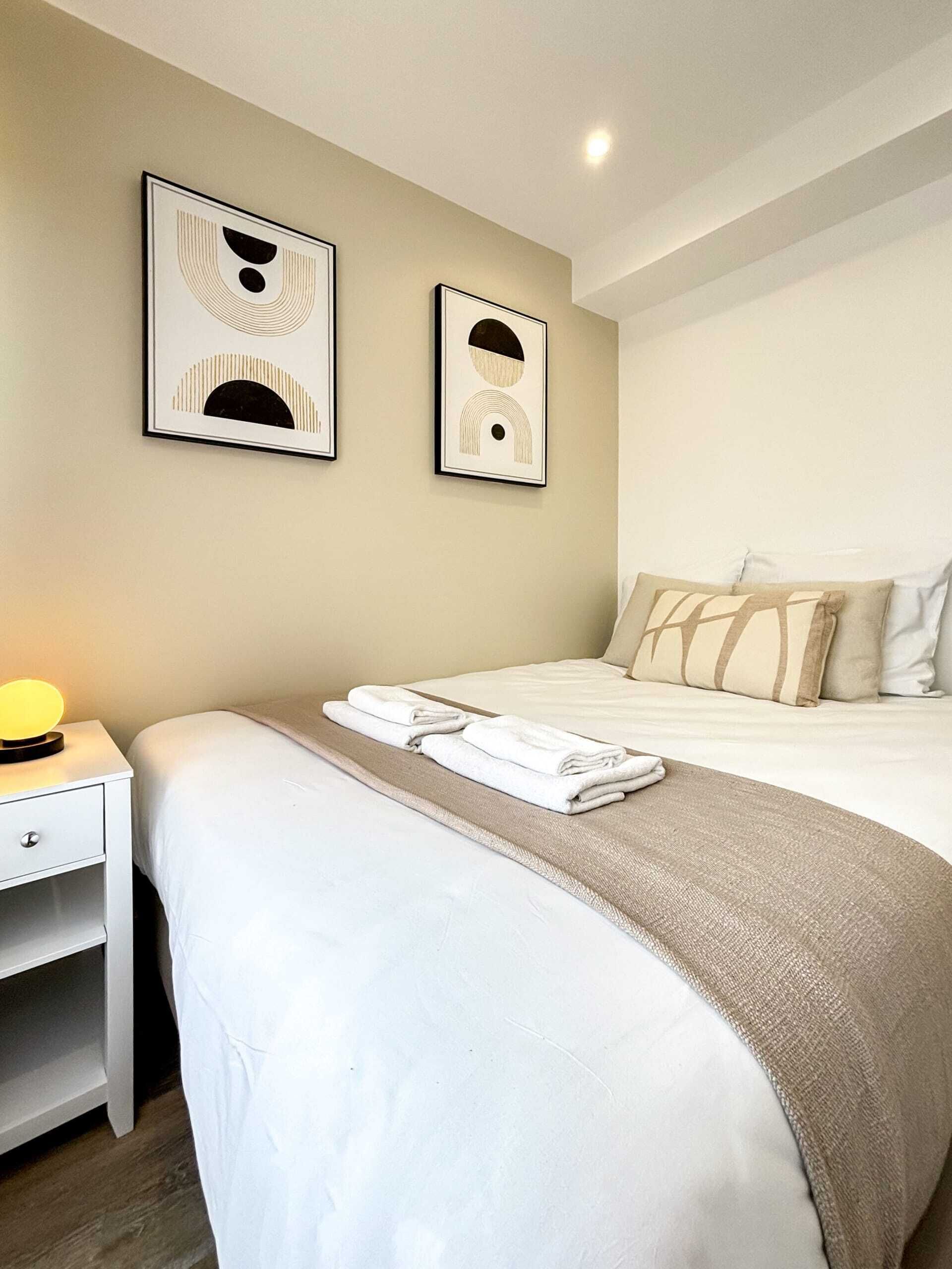 Une chambre d’hôtel avec un lit soigneusement fait, une table de chevet avec une lampe et deux œuvres d’art abstraites accrochées au mur.
