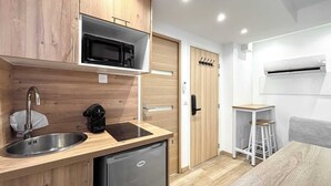 Eine kompakte Küche mit Holzschr änken, einem Edelstahl-Spülbecken, einer schwarzen Mikrowelle, einem kleinen Kühlschrank und einem weißen Klimagerät.