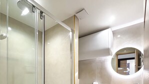 Ein modernes Badezimmer mit Glasdusche, Toilette und einem Holzkosmetikschrank mit rundem Spiegel.