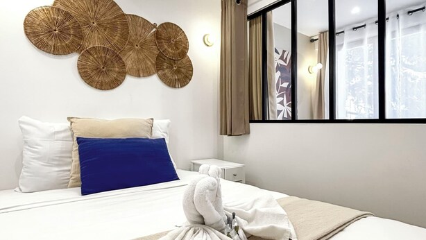 Ein modernes Hotelzimmer mit einem ordentlich bezogenem Bett, einem großen Fenster mit Vorhängen und einem an der Wand befestigten Dekorationselement.