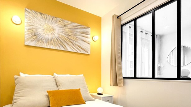 Ein modernes Hotelzimmer mit einem großen Bett, einer gelben Akzentwand und einem großen Fenster.