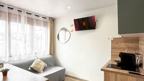 Ein modernes, kompaktes Wohnzimmer mit Küchenzeile, einer Couch und einem Spiegel sowie einem an der Wand befestigten Flachbildfernseher.