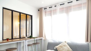 Ein modernes Wohnzimmer mit einem grauen Sofa, einem kleinen Tisch mit Hockern, einem großen Spiegel und transparenten Vorhängen.
