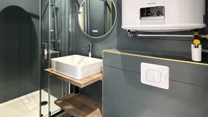 Ein modernes Badezimmer mit einer in Glas abgeschirmten Dusche, einem weißen Waschbecken und einem großen, weißen Warmwasserbereiter.