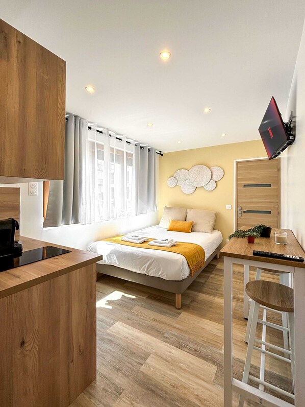 A modern hotel room with a bed, a desk, a TV, and a small kitchenette.
