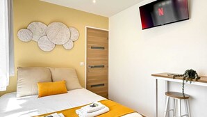 A hotel room with a bed, a desk with a chair, a TV mounted on the wall, and a door. - Hoche A 12 - Studio Apartment, Sleeps 2 (Paris)