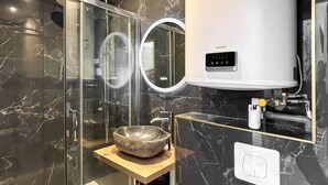 A modern bathroom with a glass shower enclosure, a marble-tiled wall, a built-in sink, and a wall-mounted heater. - Hoche A 12 - Studio Apartment, Sleeps 2 (Paris)