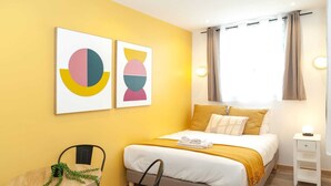 Une chambre d’hôtel comprenant un lit, une table de chevet, une chaise et deux œuvres d’art murales.
