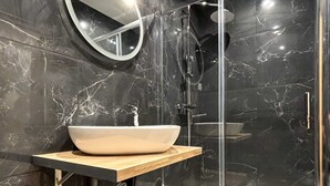Une salle de bain moderne avec un sol en marbre, un miroir rond, un meuble-lavabo en bois et une douche à parois de verre.