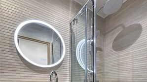 Een moderne badkamer met een ronde spiegel, een houten wastafelmeubel, een glazen douchecabine en een witte badkuip.