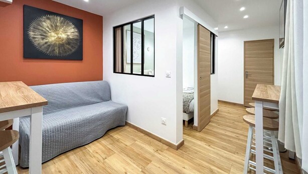Een moderne kamer met een houten vloer, een grijze bank, een houten tafeltje, een schilderij aan de muur en een schuifdeur.