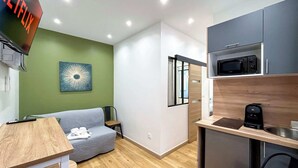 Ein kompakter Wohnraum mit Küchenzeile, einem grauen Sofa, einem Holztisch und einem an der Wand befestigten Fernseher.