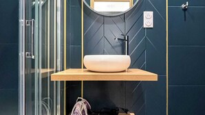 Ein modernes Badezimmer mit Duschkabine aus Glas, einem runden Spiegel und einem Holzboden mit Waschbecken.