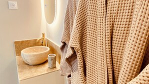 Un baño con un lavabo redondo, un espejo y un perchero con una bata colgada.