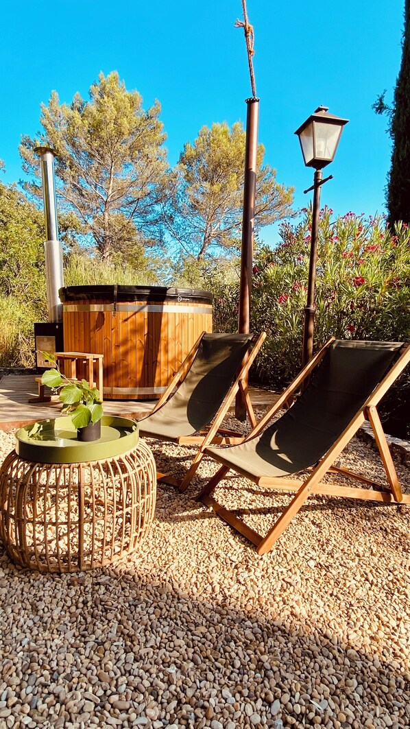 An outdoor seating area with lounge chairs, a wooden table, and a hot tub.
