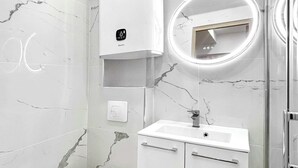Et moderne badeværelse med toilet, håndvask og et spejl med cirkulær belysning.