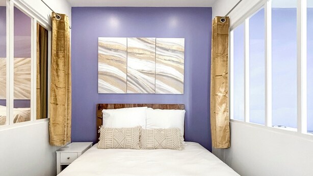 A modern bedroom with a bed, a nightstand, a wall art piece, and a window with curtains.