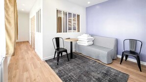 A modern hotel room with a grey sofa, two black chairs, a small round table, and a grey rug.