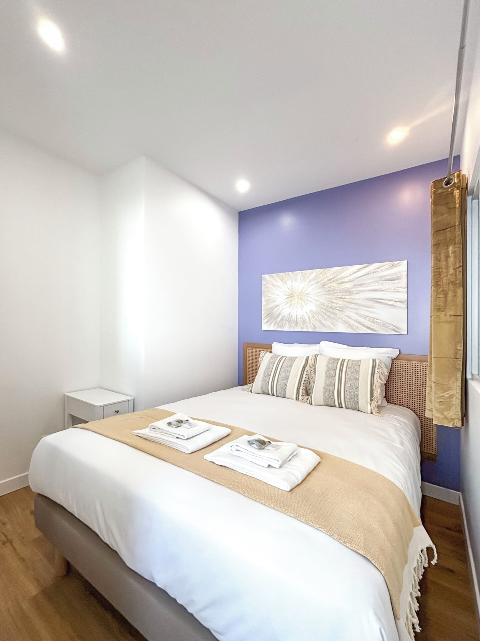 Ein modernes Hotelzimmer mit einem großen Bett, einem kleinen Nachttisch und einem an der Wand befestigten Kunstwerk.