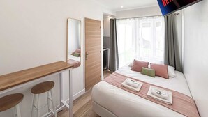 A modern hotel room with a bed, a desk with two stools, a large mirror, and a TV mounted on the wall displaying the Netflix logo. - Hoche C 105 - Studio Apartment, Sleeps 2 (Paris)