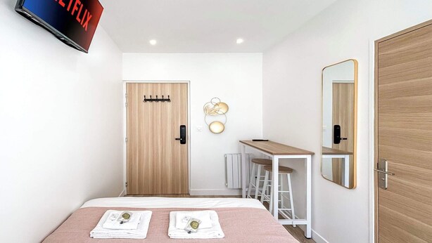 A modern hotel room with a bed, a desk, and a TV mounted on the wall. - Hoche C 105 - Studio Apartment, Sleeps 2 (Paris)