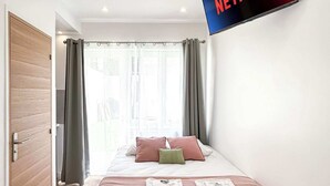 A modern hotel room with a bed, a flat-screen TV mounted on the wall, and a wooden door. - Hoche C 105 - Studio Apartment, Sleeps 2 (Paris)