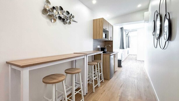 Eine moderne Küche mit einer Holzausziehtafel, weißen Barhocker und einer dekorativen Wanddekoration.