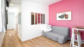 Ein modernes Wohnzimmer mit grauem Sofa, einer Wand in Rosa und Holzboden.