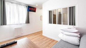 Ein modernes Wohnzimmer mit großem Fenster, einer Couch, einer Fernbedienung und einem Netflix-Logo.