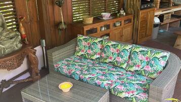 A covered outdoor seating area with wicker furniture, a wooden table, and a grill.